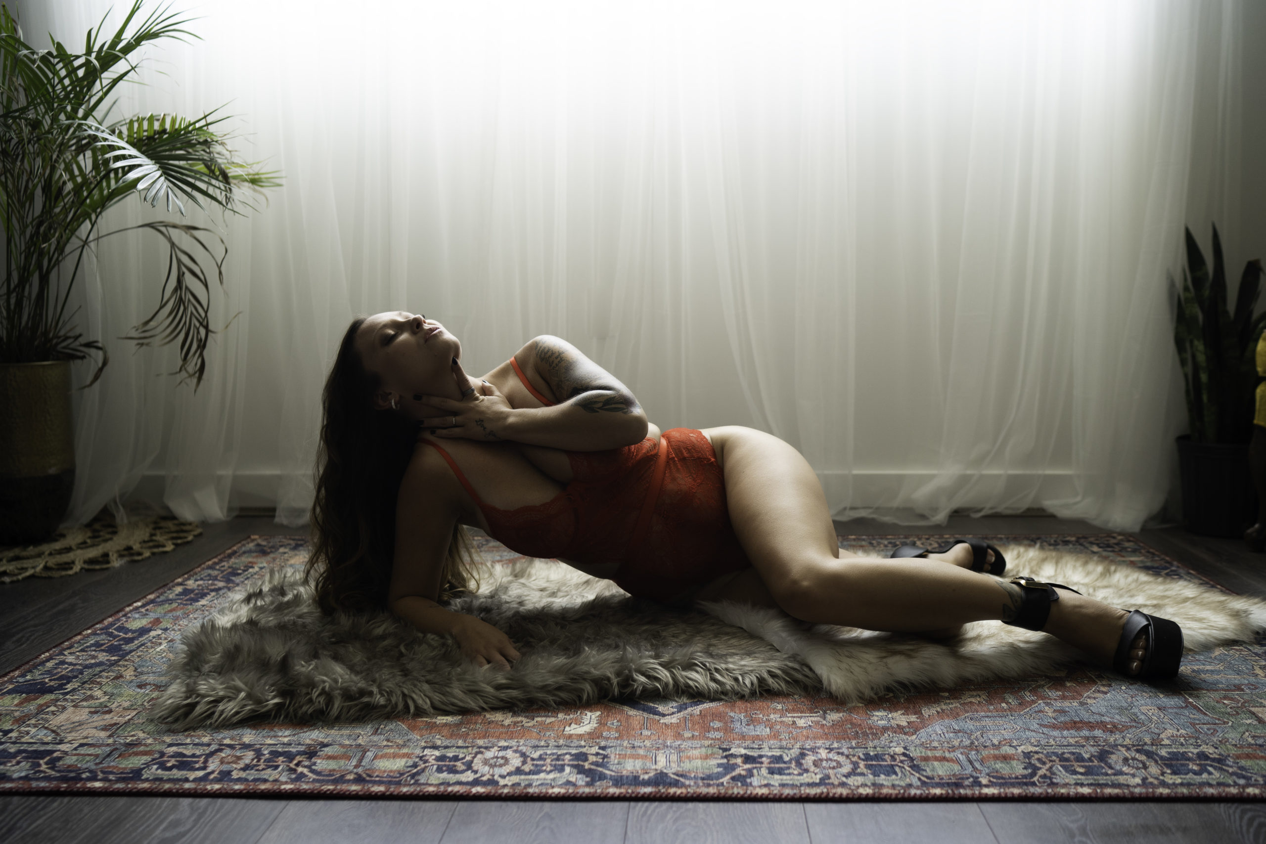 woman laying on the floor on her side with her hand around her throat in red lingerie.