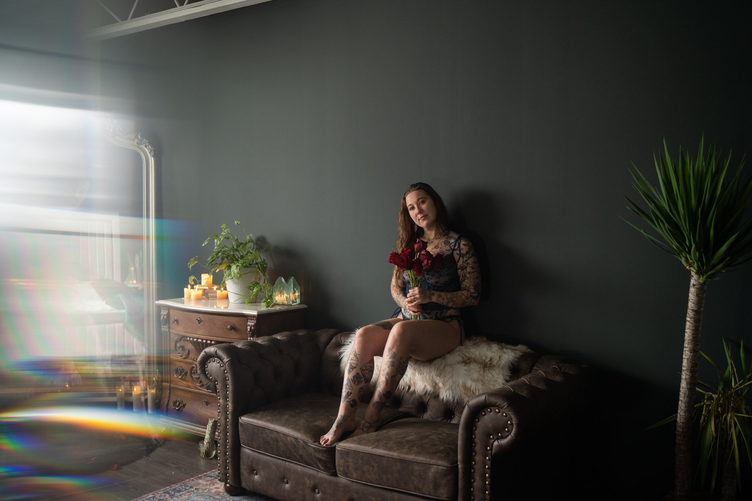 woman sitting on the back of the couch holding a bouquet of roses during her boudoir session