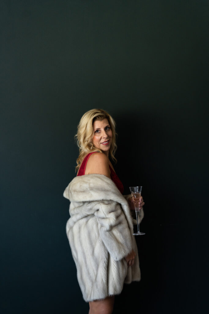 woman wearing a fur coat holding a waterford crystal champagne glass in red lingerie during her shoot with Magan Rogers, Michigan Boudoir Photographer.