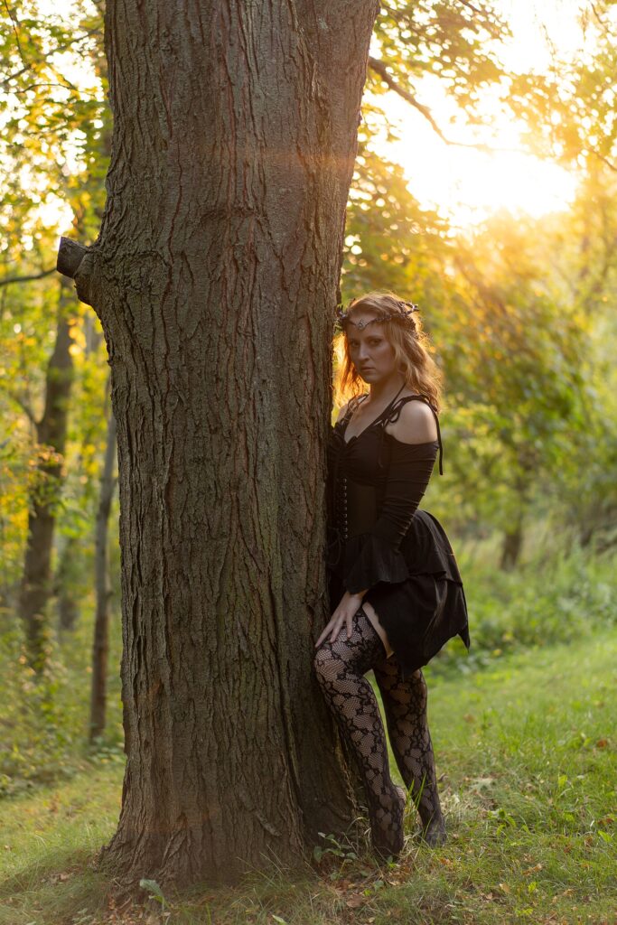  woman looking sultry and mysterious behind a tree in the woods.