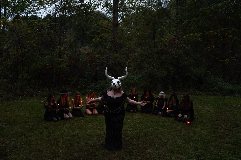 Woman wearing a skull mask leads a powerful witchy ritual surrounded by women holding candles.