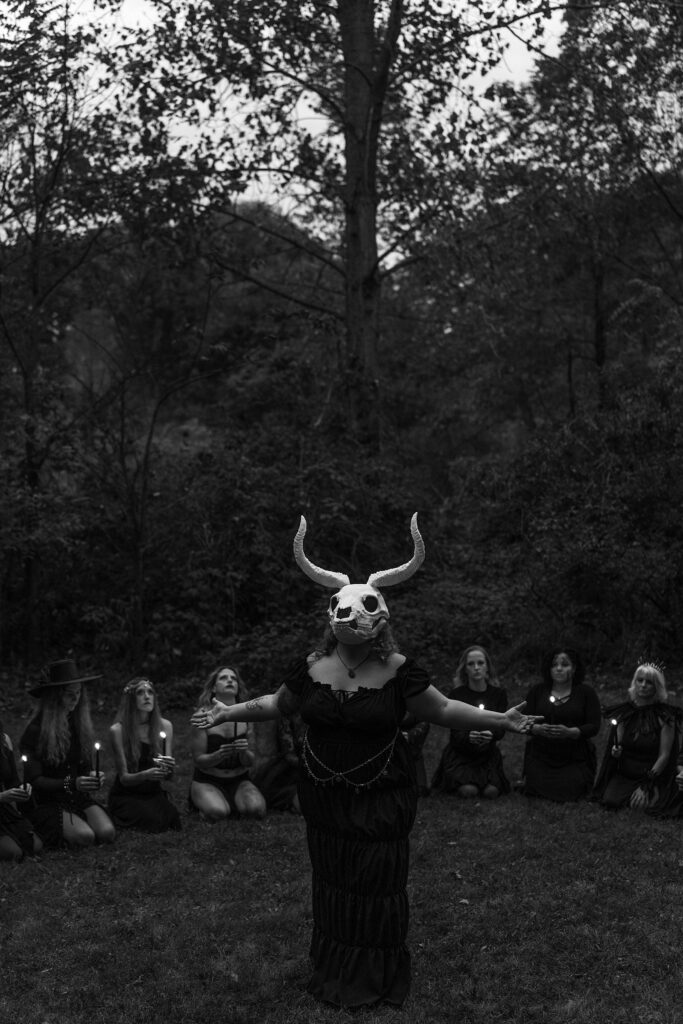 Women gathered around a skull masked leader in a ritual type setting.