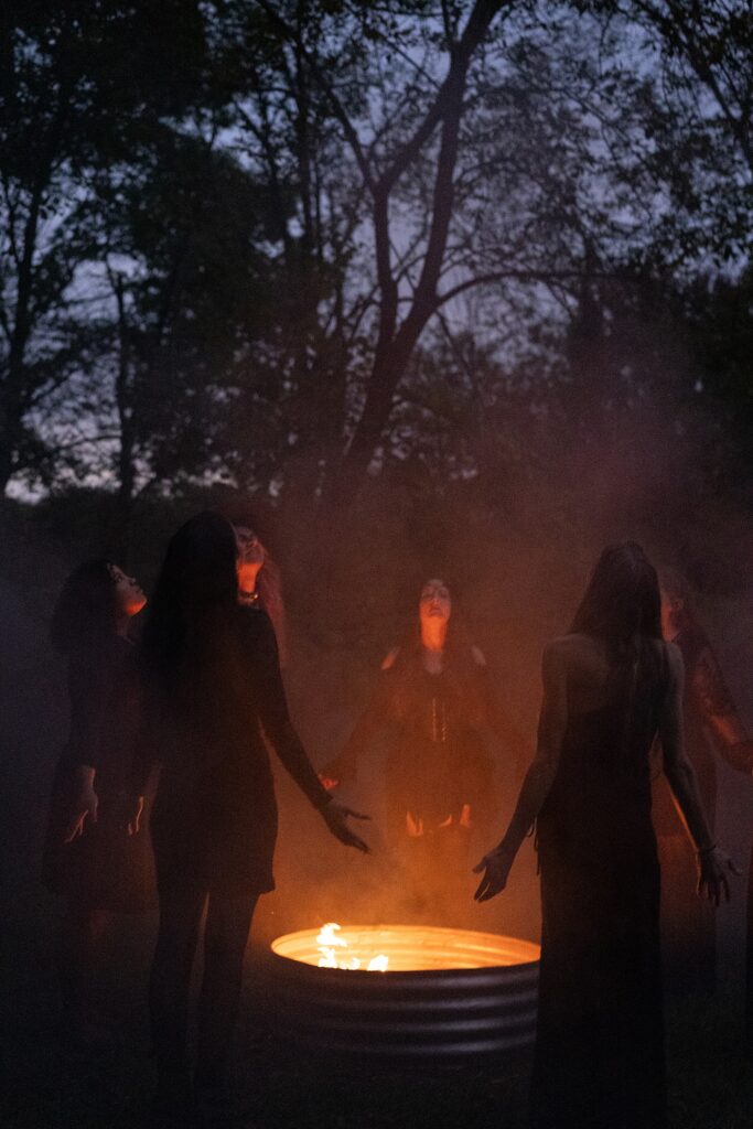 Women in black dresses dancing around a fire during a witchy boudoir session celebrating feminine power.